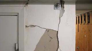 Stora sprickor i väggen visar behovet av att laga sprickor i grunden. En metallplatta med bult sitter fast i den spruckna väggen.